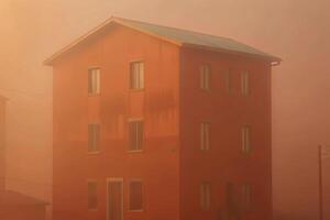 Orange building in hazy morning fog, three stories tall with many windows photo