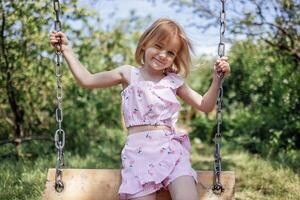Little girl is rocking on swing in summer garden photo