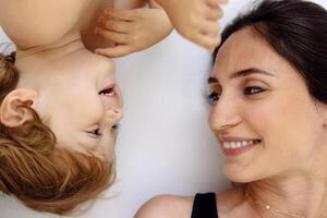 A close-up portrait in profile of a laughing mother and a cute child. A smiling woman and her little son are lying on a white floor. photo