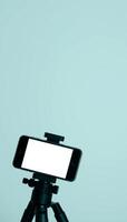 A smartphone mounted on a tripod, positioned against a muted blue background, emphasizing functionality for filming and streaming purposes in content production. photo
