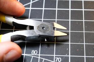 Fingers holding stainless nipper for cutting plastic. Black Cutting mat background with white lines. The concept of a master model kits hobby. Negative space. Sharp pliers photo