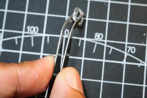 A hand on black cutting mat holds a Tweezer for pinching tiny parts. Black Cutting mat background with white lines. The concept of a master model kits hobby. Negative space photo