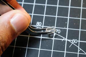 A man's hand on black cutting mat holds a Tweezer for pinching tiny parts. Black Cutting mat background with white lines. The concept of a master model kits hobby. Negative space photo