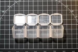 Mini transparent container on black striped cutting mat. Four small containers for storing tiny parts. Model kits and robotic build hobbies. Plastic equipments. Isolated objects on black backgrounds photo