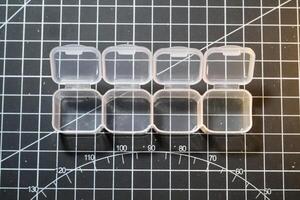 Mini container set on black striped cutting mat. Four small containers for storing tiny parts. Model kits and robotic build hobbies. Plastic equipments. Isolated objects on black photo