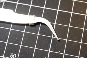 Metal precision tweezer with pointed tip. Tweezer is on a black cutting mat with lines. A tool that functions to clamp and pull out small objects. Negative Space. photo