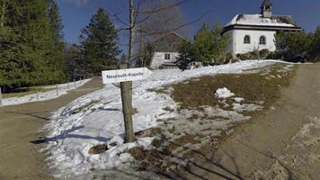 Tegernsee, Germany. Neureuth Kapelle am Tegernsee in spring on snowy day. Small white chapel on hill next to Neureuth alp above Tegernsee lake. Small church on top of mountain. video