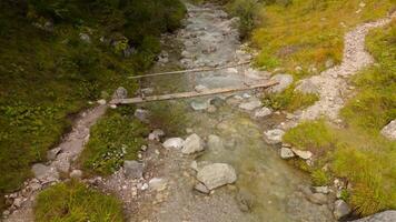 Breathtaking aerial shot of Bavarian Alps, featuring a charming wooden bridge over a tranquil mountain stream, nestled in a forest of colorful autumn leaves and rugged rocky landscape in Germany. video