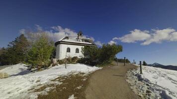 Tegernsee, Germany. Neureuth Kapelle am Tegernsee in spring on snowy day. Small white chapel on hill next to Neureuth alp above Tegernsee lake. Small church on top of mountain. video