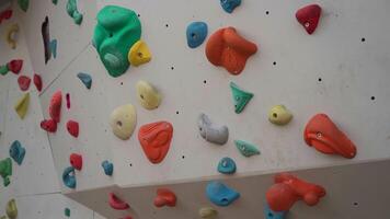 Climbing wall with grips in bouldering center. Wall of an empty indoor rock climbing gym. Boulder cliff with artificial rocks. Kids clamber wall with colored grips and route markers. video