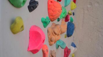 Climbing wall with grips in bouldering center. Wall of an empty indoor rock climbing gym. Boulder cliff with artificial rocks. Kids clamber wall with colored grips and route markers. video