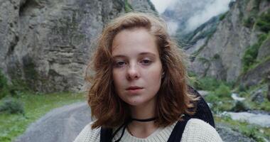 Russia, Caucasus, Elbrus. Young red-haired girl of European appearance with freckles smiling while looking at the camera, standing on a mountain road among the rocks in the daylight photo