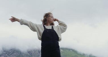 Russia, Caucasus. A beautiful young woman of European appearance, dressed in a warm sweater, stands on the parapet against the background of green hills and makes smooth movements with her hands photo