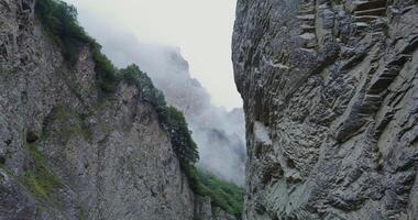 A deep crevice between sheer rocky cliffs covered with sparse vegetation. The tops of the mountains are covered with clouds photo