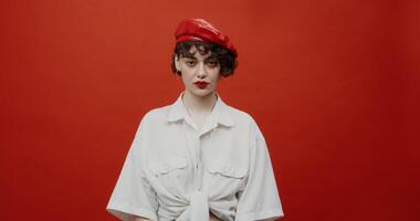 A brunette woman of European appearance with a short haircut in a red panama hat looks at the camera with a bored look. Shooting on a red background. photo