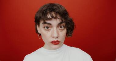 A short-haired brunette of European appearance with red lipstick is staring straight into the camera while chewing gum. Shooting on a red background. photo