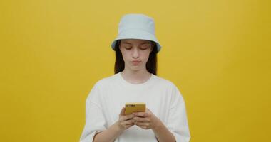 A beautiful young woman of European appearance in a panama hat smiling, chatting on a mobile phone. Portrait videography with a solid yellow background photo
