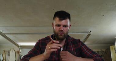 a serious man of European appearance with a beard, in a plaid shirt, is actively talking while looking at camera and gesturing with his hands in a carpentry workshop, a lot of wooden products photo