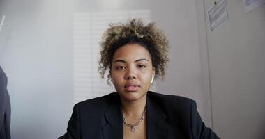 black-skinned girl with an African hairstyle in a black business jacket with, an earring in the nose and a chain around her neck with headphones in her ears is seriously looking at the camera close-up photo