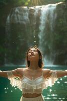 A woman in a white dress standing in front of a waterfall photo