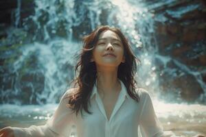 A woman in white shirt standing in front of a waterfall photo