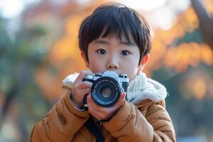 A young boy holding a camera in front of a tree photo