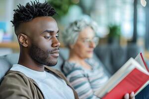 A man reading a book while sitting next to an older woman photo