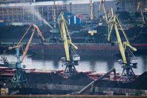 Bustling Industrial Port Cargo Ships moored along Docks, with large Cranes actively loading and unloading coal. Maritime Logistics, heavy machinery, and importexport industry in a waterfront setting photo