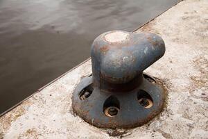 Rustic Metal Mooring Bollard mounted on Concrete Pier water, providing secure Docking for Boats. Weathered metal, aged surface, industrial setting emphasize functional enduring nature infrastructure photo