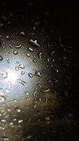 Rain Droplets at Night on Wet Windshield Near Streetlight photo