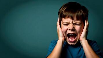 A portrait of a dark-haired boy screaming and covering his ears with both hands, on dark green background with empty space for text on the left, for banners, cards or messages photo