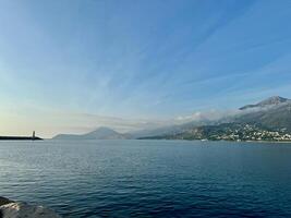 A panoramic view of Bar, Montenegro, in warm pre-sunset light with clear blue sky snd seascape, a distant horizon line, a lighthouse, and mountains in the background photo