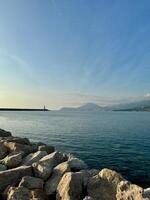 Vertical view of Bar, Montenegro, in warm sunset light with clear blue sky snd seascape, a distant horizon line, a lighthouse, and mountains in the background photo