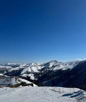 Vertical aerial view of the snow-covered mountain peaks in Bakuriani, Georgia, clear blue sky, with space for text, for cards and banner photo