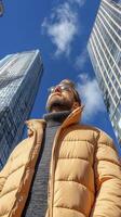 Man in Tan Puffer Jacket Looks Up at City Skyscrapers photo