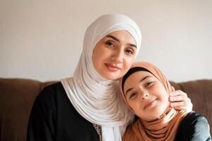 Portrait of a happy Muslim family at home young mother and child daughter in hijab looking at camera and smiling. photo