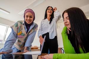A group of diverse female college students studying together or a young happy business team of three woman working together on a project plan in the office workplace. photo