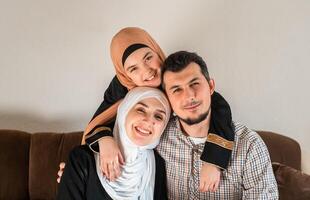 Portrait of a happy Muslim family at home, a young father, mother and child daughter in hijab looking at the camera and smiling. photo
