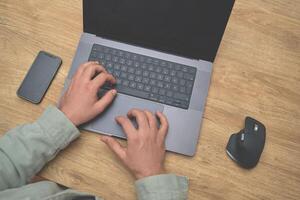 Man using a laptop on the wooden desk table top view. photo