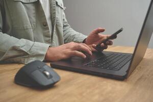 Closeup image of a man using a laptop and phone on the wooden desk table, business concept. photo