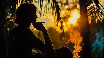 A silhouette of a man sitting in front of a palm tree photo