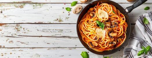 Spaghetti with mushrooms and tomatoes in a pan on a white wooden table photo