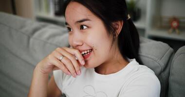 Handheld selective focus shot, Young woman is sitting on a sofa, smiling happily while thinking about something in the living room at home. video