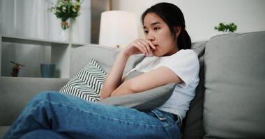 Handheld low angle view shot, Stressed Asian woman sitting on the sofa, thinking and worrying about something in the living room at home. A sad and exhausted moment. video