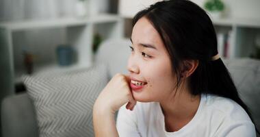 Handheld shot, Asian woman sits on a sofa relaxed and smiles happily after hearing something that makes her feel good or relieved. video