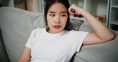 Handheld high angle view shot, Asian woman leaning against sofa as if thinking or worrying about something in living room at home. Facial expression concept video
