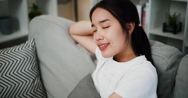 Handheld high angle view shot, Attractive young woman is sitting on a sofa leaning against a soft pillow, her eyes closed, and breathes in and out in relaxation. video