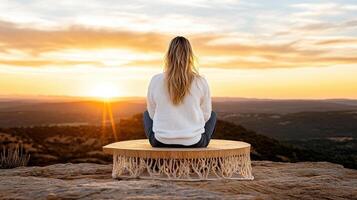 woman sitting on rock, enjoying serene sunset view over landscape photo