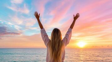 woman with long hair raises her arms in celebration against vibrant sunset over ocean photo