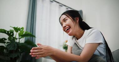 Young woman is sitting on a sofa, smiling happily while thinking about something in the living room at home. video